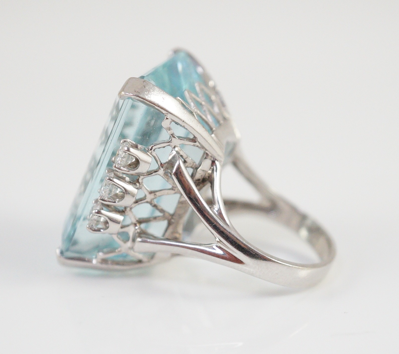 A large modern 14k white gold and emerald cut aquamarine set dress ring, flanked by six round cut diamonds